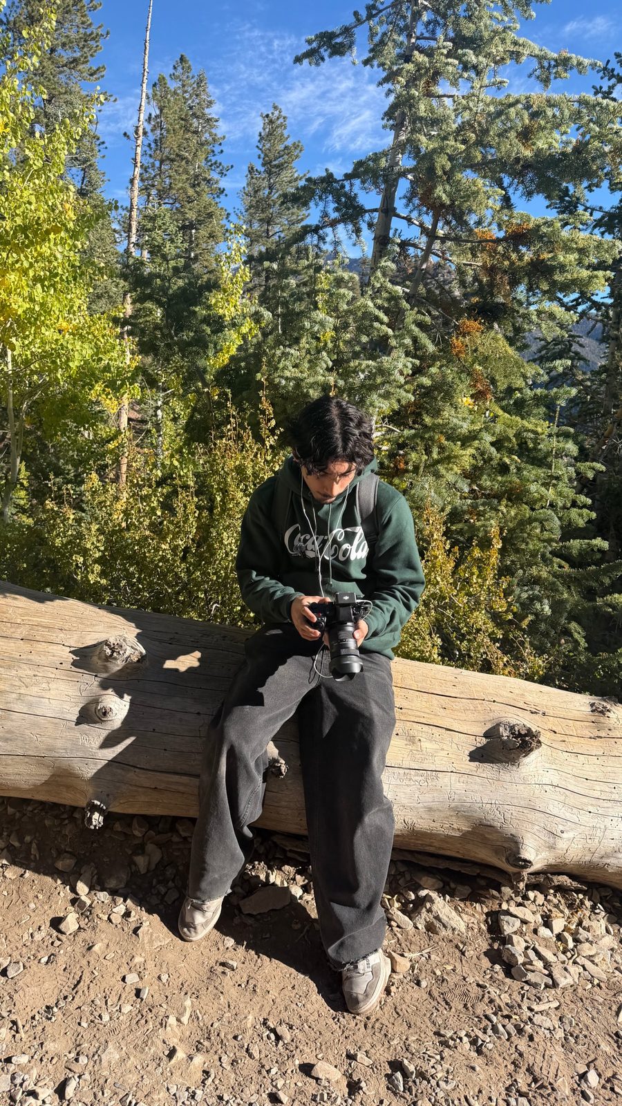 Antonio reviewing footage on his camera while sitting on a log at Mount Charleston