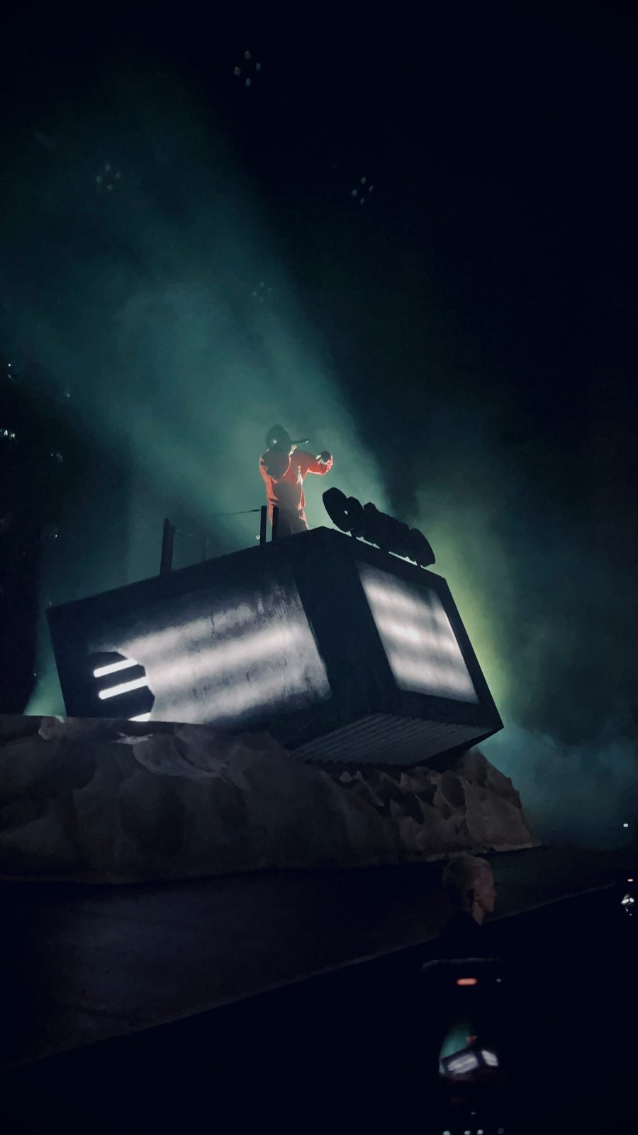 Baby Keem in a red outfit performing on top of a tilted stage set, lit by green haze